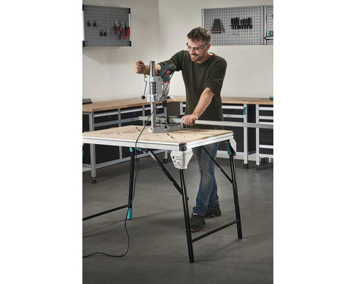 Man werkt met een boormachine aan een werkbank in een werkplaats.