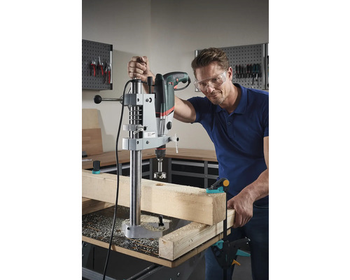 Man boort met een boormachine en boorstandaard een gat in een stuk hout.