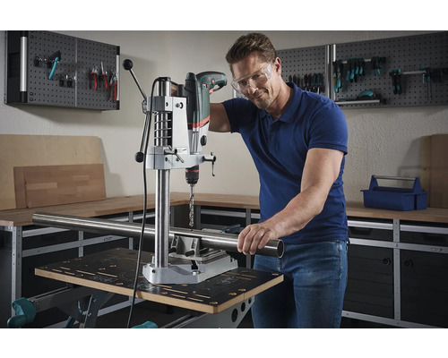 Een man boort met een tafelboormachine een pijp in een werkplaats.