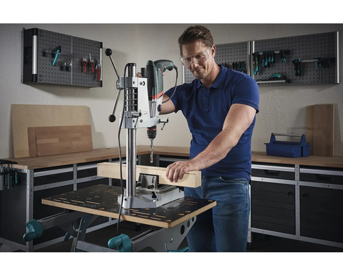 Man werkt met een kolomboormachine aan een stuk hout in een werkplaats