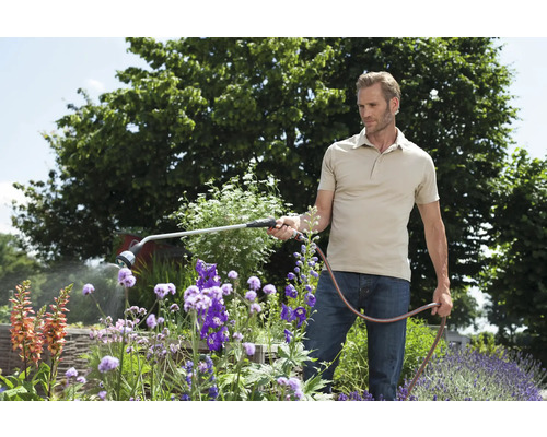 Man besproeit bloemen met een tuinspuit in de tuin.