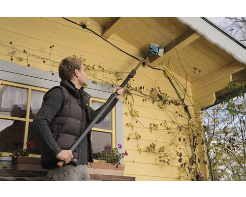 Iemand maakt een dakgoot schoon met een dakgootborstel.