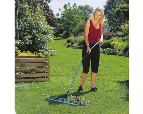 Vrouw harkt gras met een bladhark in de tuin