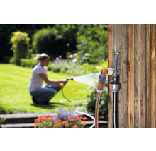 Tuinscène met slangconnector en kraanaansluiting op een houten wand, een vrouw besproeit de tuin