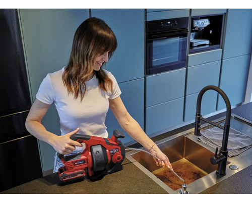 Vrouw gebruikt een ontstoppingsveer van Einhell om een afvoerpijp te ontstoppen.