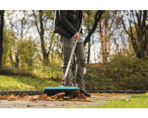 Een persoon veegt bladeren met een straatbezem buitenshuis.