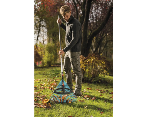 Een man harkt bladeren met een bladhark in de tuin.