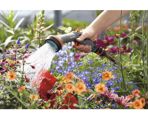 Een hand houdt een tuinspuit vast en bewaterd bloemen.
