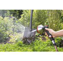 Iemand reinigt een vuile schop met een Gardena sproeier in de tuin.