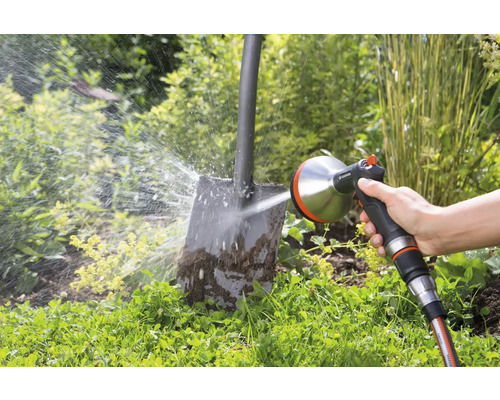 Iemand reinigt een vuile schop met een Gardena sproeier in de tuin.