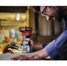 Een man werkt met een Einhell accu bovenfrees op een stuk hout. Er is een afzuiginstallatie aangebracht.