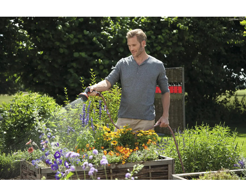 Een man bewatert bloemen met een tuinslang in de tuin.
