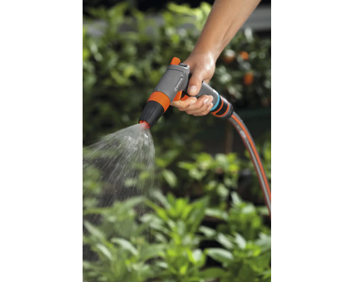 Een hand houdt een tuinspuit vast die water sproeit.