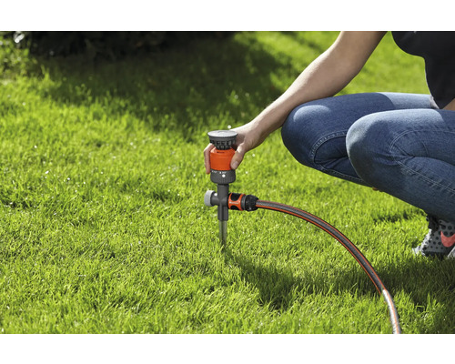 Een persoon stelt een gazonsproeier af op een gazon.