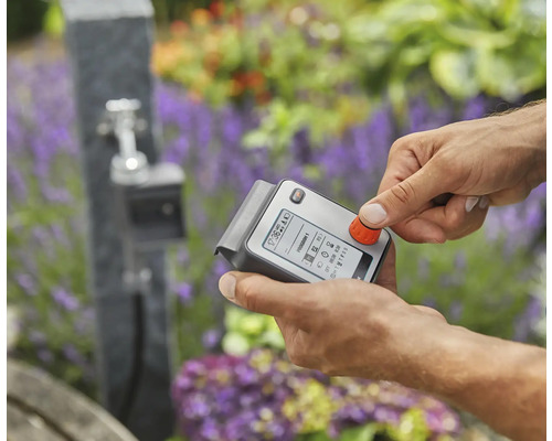 Iemand bedient een elektronische irrigatiecomputer voor de tuin.