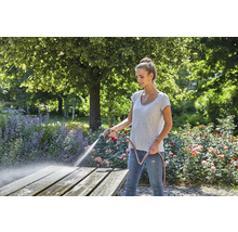 Vrouw reinigt houten tafel met tuinslang in de tuin