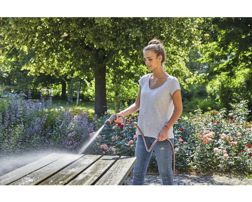 Vrouw reinigt houten tafel met tuinslang in de tuin