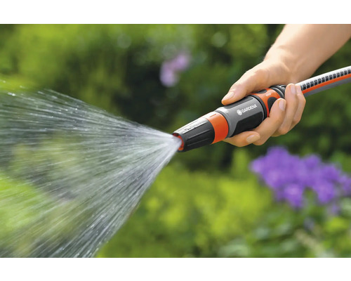 Een hand houdt een Gardena tuinslang vast waar water uit spuit.