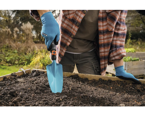 Persoon met tuinhandschoenen gebruikt een tuinschep in een verhoogde tuinbak.