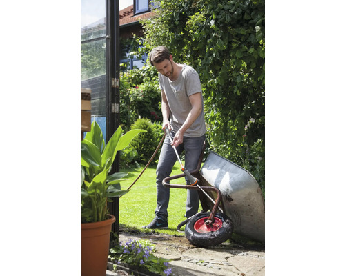 Man reinigt een kruiwagen met een tuinslang in de tuin.