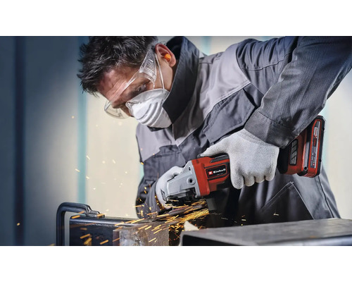 Een man slijpt metaal met een Einhell accu-haakse slijper en draagt beschermende kleding.