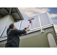 Man reinigt glazen borstwering met een draadloze ruitenreiniger.