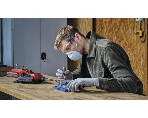 Een man werkt met een draadloos multifunctioneel gereedschap, beschermd door veiligheidsuitrusting.