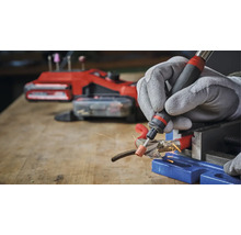 Persoon slijpt metaal met een multifunctioneel gereedschap en beschermende handschoenen in een werkplaats.