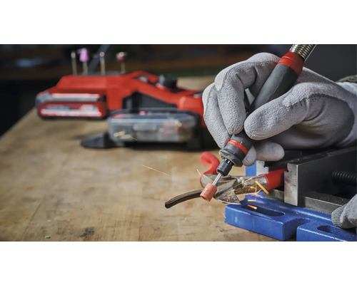 Persoon slijpt metaal met een multifunctioneel gereedschap en beschermende handschoenen in een werkplaats.