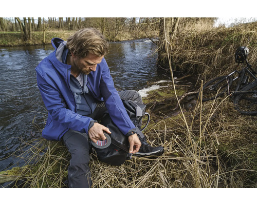 Man met tape aan de oever van een rivier, naast een fiets.