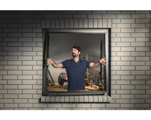 Man opent een kiepraam in een bakstenen huis.