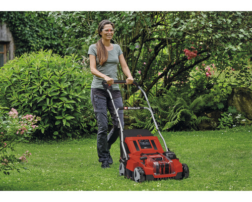 Vrouw bedient een rode Einhell grasmaaier in de tuin.