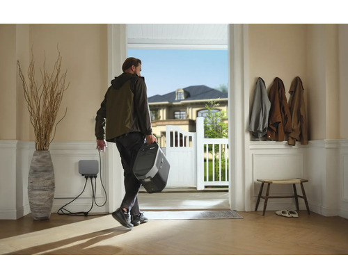 Persoon verlaat het huis met een draagbaar powerstation, aangesloten op een wandlaadstation