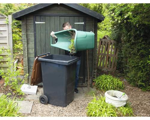 Man leegt groenafval in een afvalcontainer in de tuin