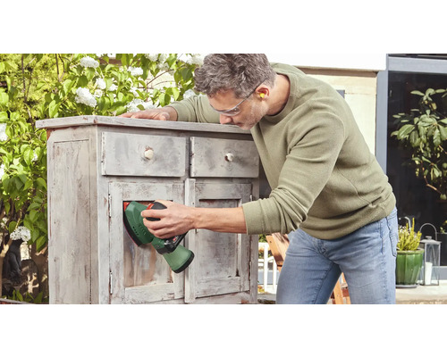Man schuurt een houten meubelstuk buitenshuis met een schuurmachine.