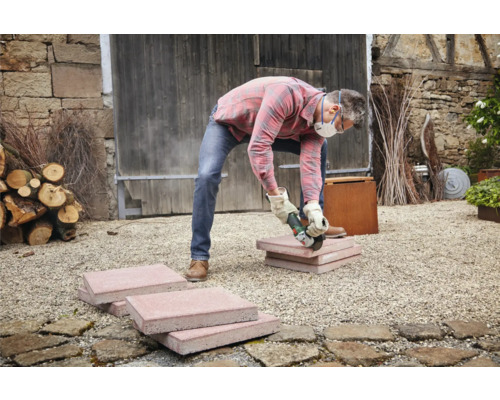 Ambachtsman snijdt straatstenen met een haakse slijper in de buitenlucht.