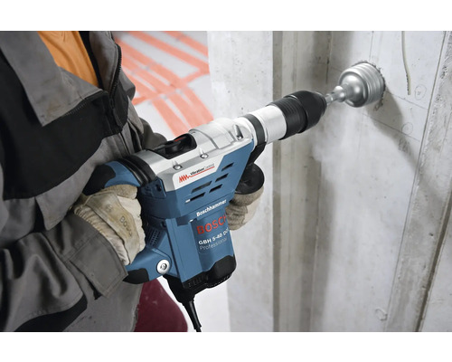 Een man boort met een Bosch boorhamer een gat in een betonnen muur.