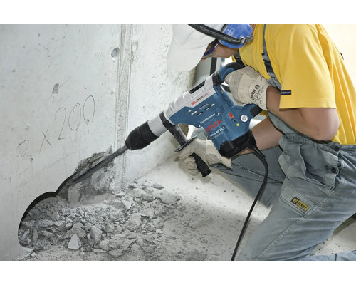 Een arbeider gebruikt een breekhamer om een gat in een betonnen muur te boren.