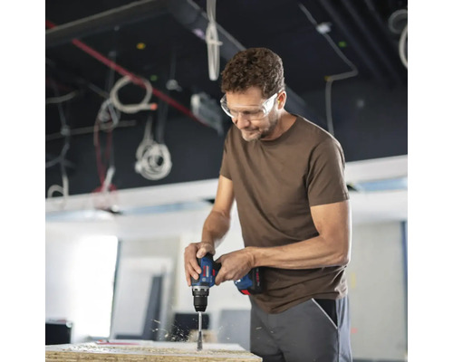 Een man boort met een boormachine een gat in een houten plank.