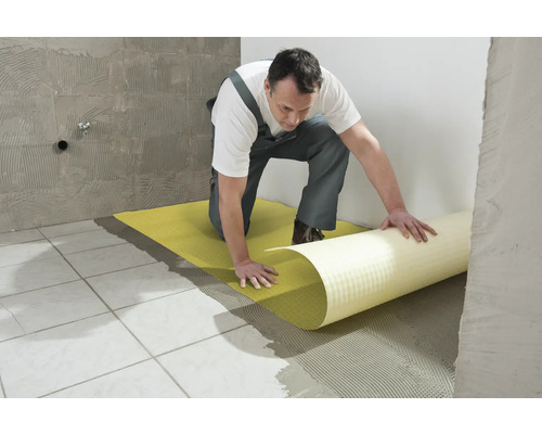 Een man legt een ontkoppelingsmat op een betegelde vloer.