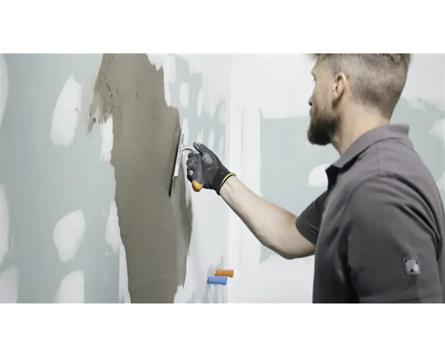 Man plamuurt muur met vulmiddel