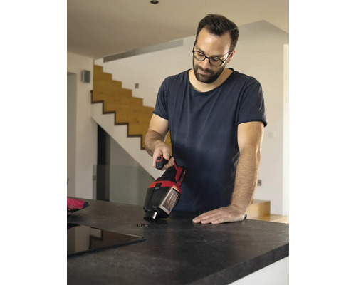 Een man gebruikt een draadloze kruimelzuiger op een aanrecht om vuil te verwijderen.