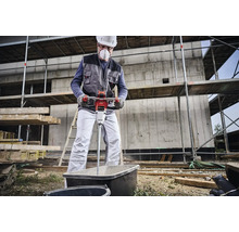 Een bouwvakker mengt mortel met een elektrische mortelmixer in een kuip op een bouwplaats.