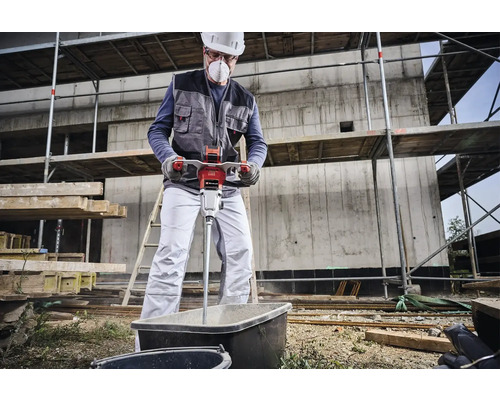 Een bouwvakker mengt mortel met een elektrische mortelmixer in een kuip op een bouwplaats.
