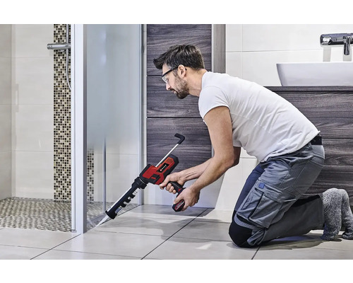 Klusjesman gebruikt een accukitspuit in de badkamer om een douchecabine af te dichten.