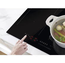 Een persoon bedient een zwarte inductiekookplaat met een pan groenten erop.