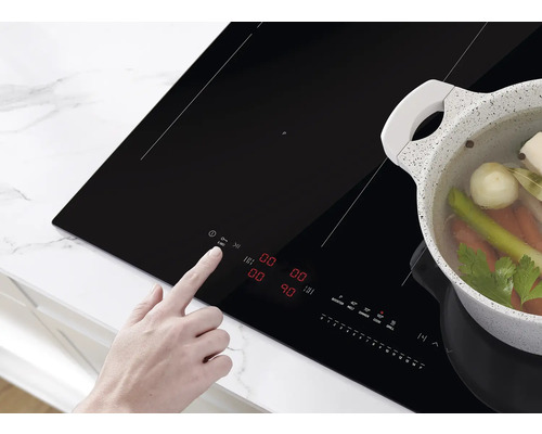 Een persoon bedient een zwarte inductiekookplaat met een pan groenten erop.