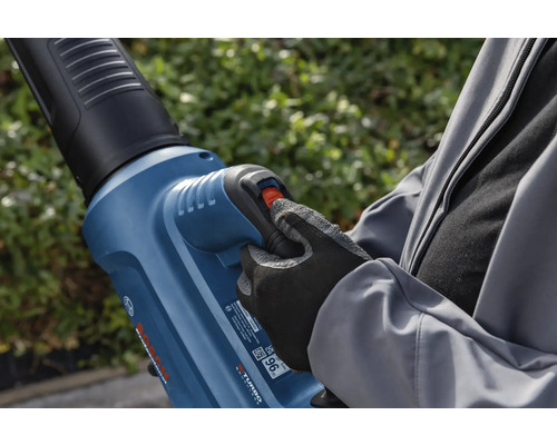 Een persoon bedient een bladblazer in de tuin.