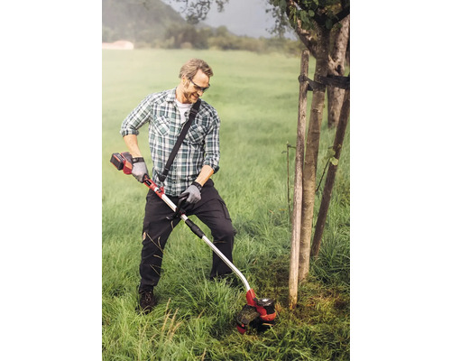 Een man trimt gras met een accugrastrimmer in een tuin.