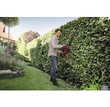 Een man snoeit met een heggenschaar een heg in een tuin.